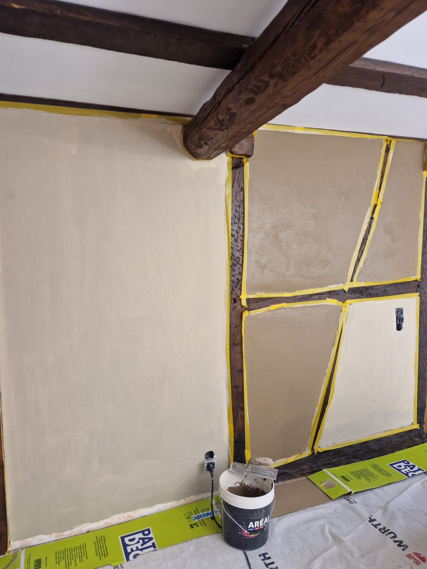 Avant - Couloir Mur inachevé avec sections crépies, délimitations jaunes et seau de peinture.