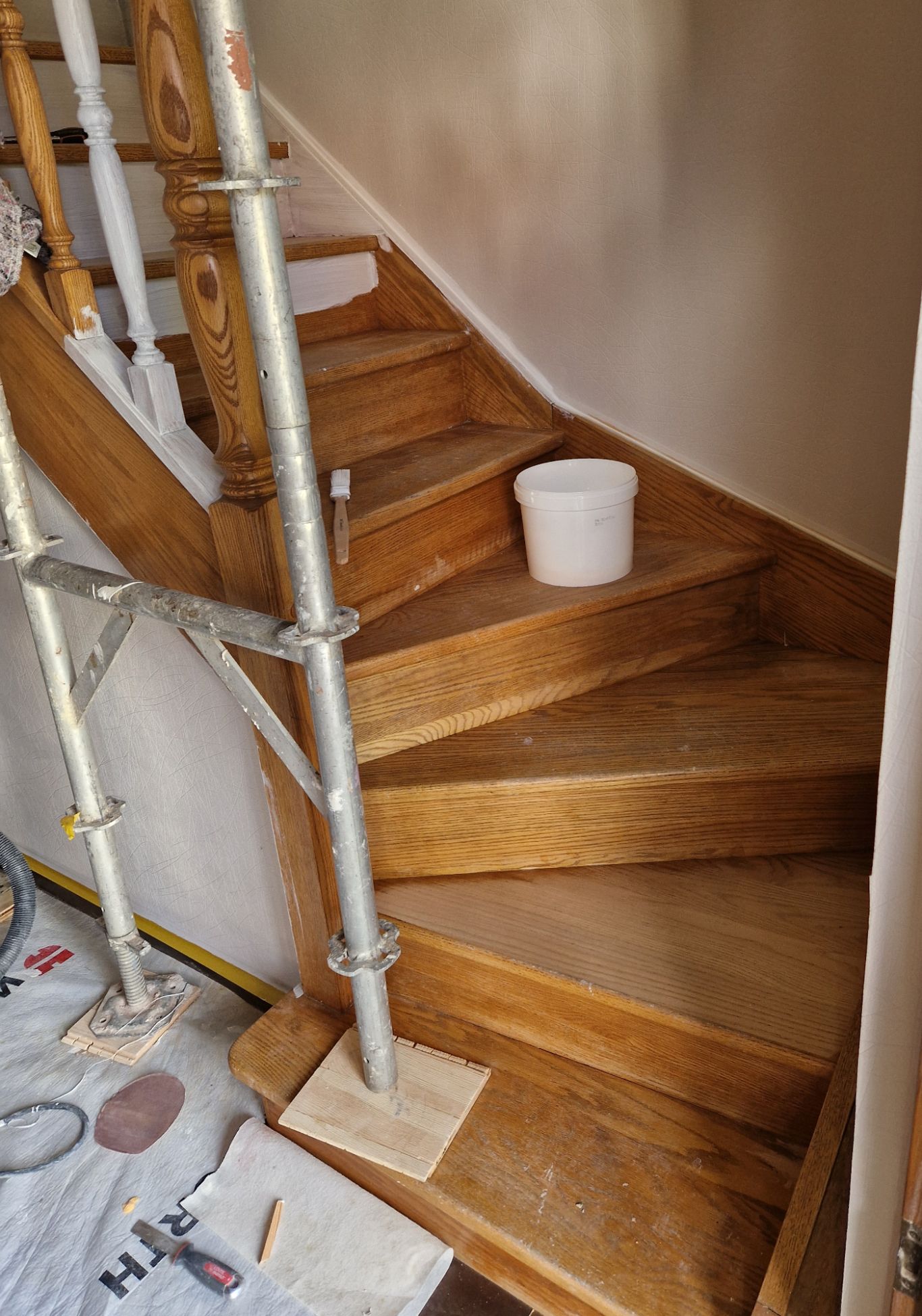 Avant - Escalier classique Échelle en bois partiellement rénovée avec des échafaudages et un seau en bas.