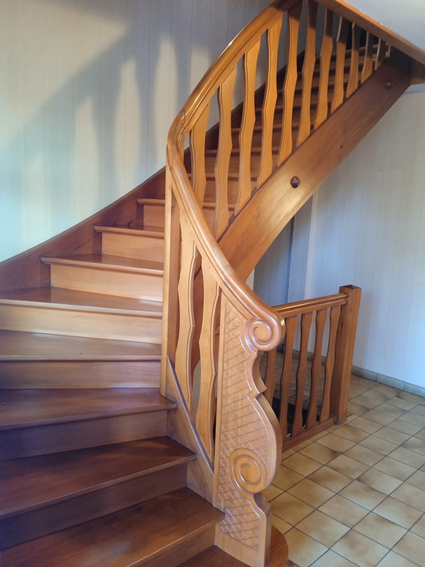 Avant - escalier bois Escalier en bois sculpté avec rambarde, lumière naturelle.