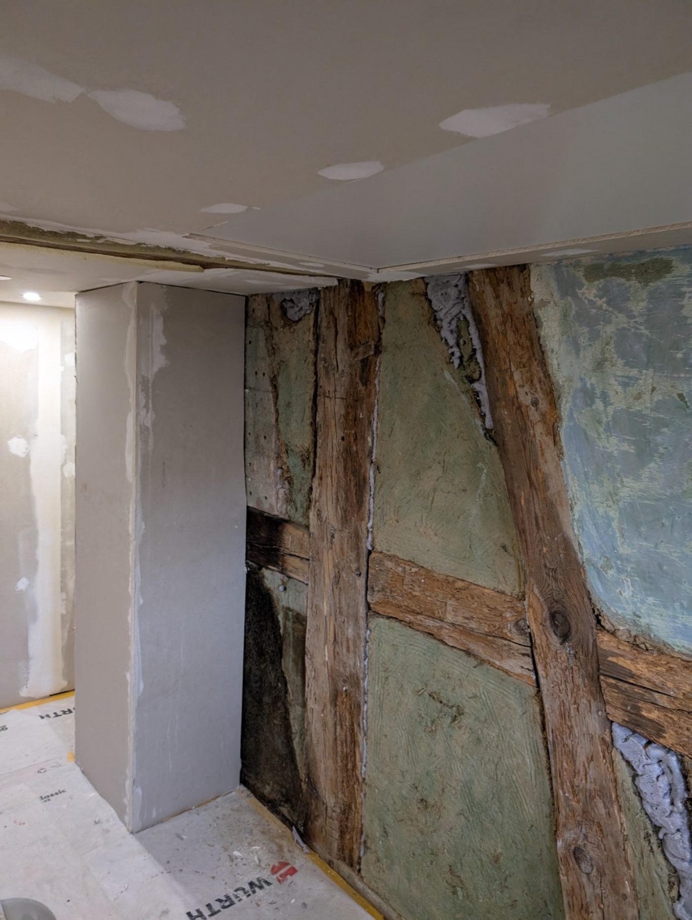 Avant - Mur colombage Intérieur d'une pièce en rénovation avec murs en plâtre et poutres en bois exposées.